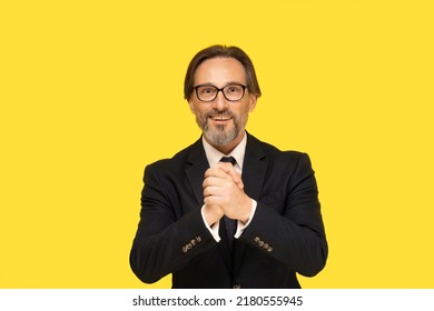 Gesturing All The Best With Hands Handsome Middle Aged Businessman Looking At Camera Isolated On Yellow Background. Handsome Mature Businessman In Black Suit And Eye Glasses. Business Concept.