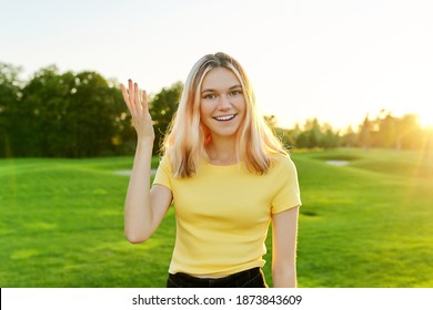 Gesturing Young Beautiful Female Teenager Talking At Camera, Student 16, 17 Years Old Giving Interview Looking At Camera, Green Sunset Lawn In Park Background