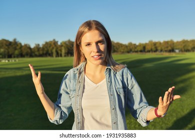 Gesturing young beautiful woman talking at camera, female in denim shirt, teenager student giving interview looking at camera, road in park sunset summer day background - Powered by Shutterstock