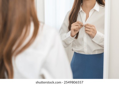 Get dress, beautiful asian young woman, businesswoman standing buttoning white shirt formal getting dressed, ready before go to work looking reflection the mirror in bedroom in the morning at home. - Powered by Shutterstock