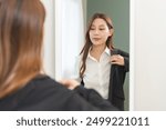 Get dress, pretty asian young woman, businesswoman standing wearing suit formal with shirt, female getting dressed preparing before go to work looking reflection in the mirror in the morning at home.