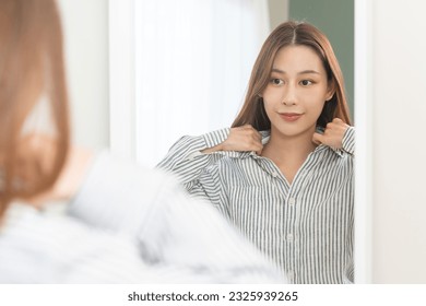 Get dress, pretty asian young woman, businesswoman standing wearing striped shirt, female getting dressed preparing before go to work looking reflection in the mirror in the morning at home. - Powered by Shutterstock