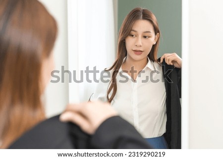 Get dress, pretty asian young woman, businesswoman standing wearing suit formal with shirt, female getting dressed preparing before go to work looking reflection in the mirror in the morning at home.