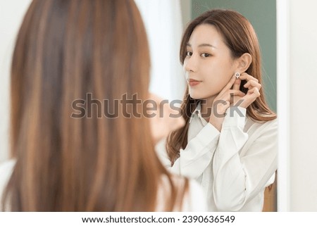 Get dress, pretty asian young woman, businesswoman standing putting earring or jewelry, wearing white shirt formal getting dressed getting ready before go to work looking reflection the mirror at home