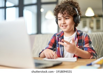Get more knowledge. Happy latin american little boy wearing headphones, looking at the screen of a laptop while communicating with his teacher during online lesson at home