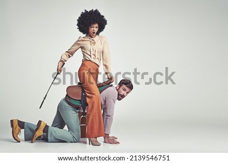 Get moving. A studio shot of an attractive woman in 70s wear riding a handsome man wearing a saddle while using a riding crop. Stock photo © 