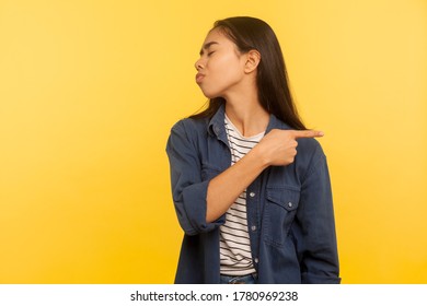 Get out, leave me! Portrait of annoyed vexed girl in denim shirt pointing way out and turning away with disrespect disgust, expressing resentment. indoor studio shot isolated on yellow background