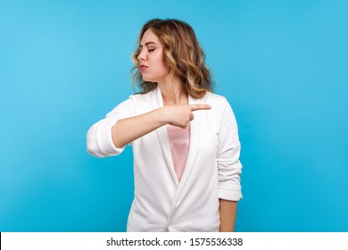 Get out! Portrait of mad bossy woman with wavy hair in white jacket pointing to the side and turning away with angry vexed face, giving order to leave. indoor studio shot isolated on blue background