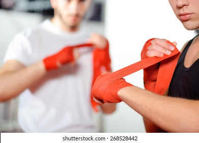 Get Prepared To The Fight. Athletic Guys Pulling On Hands Red Boxing Bandages