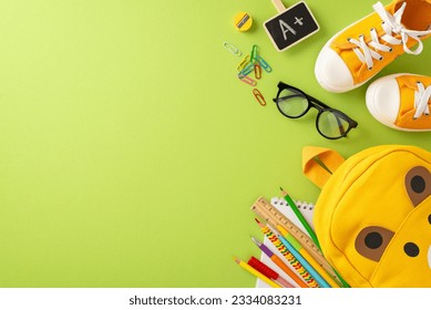 Get ready for elementary school. Top view of bear-shaped backpack, colored markers, sketchbook, art supplies, clips, glasses, A+ grade symbol, sneakers on soft green backdrop with space for text or ad