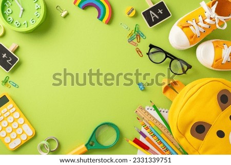 Get ready for first day of elementary school. Top view of playful bear-shaped bag, crayons, drawing pad, A+ achievement symbol, sneakers and more on soft green surface with blank frame for text or ad