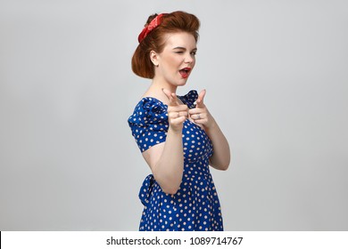 Get ready. Horizontal isolated portrait of fashionable European pin up girl wearing retro hairstyle, make up and vintage dress winking and pointing two index fingers at camera as if flirting with you