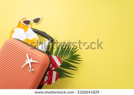 Get ready for summer! Top view of suitcase, small plane model, beach accessories, sunglasses, sunscreen, flip-flops, towel, and palm leaf against yellow background. Advertise your vacation deals here