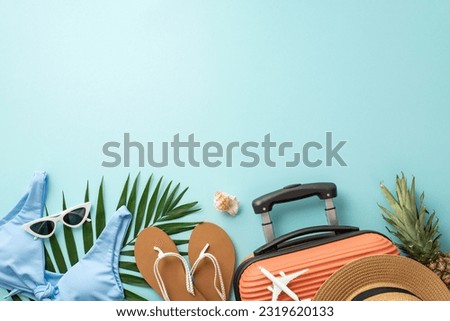 Get in vacation mode! Top view shot of suitcase, small airplane model, beach essentials, glasses, hat, flip-flops, bra, ananas, shell, palm leaves, light blue backdrop. Space available for text or ad