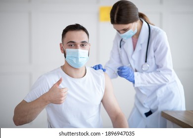 Get vaccinated. Young Caucasian guy showing thumbs up during coronavirus vaccination at clinic, promoting covid-19 immunization. Protection against global virus concept - Shutterstock ID 1896947035
