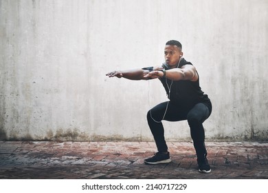 Get Your Squat On. Full Length Shot Of A Handsome Young Man Listening To Music While Exercising Outside.