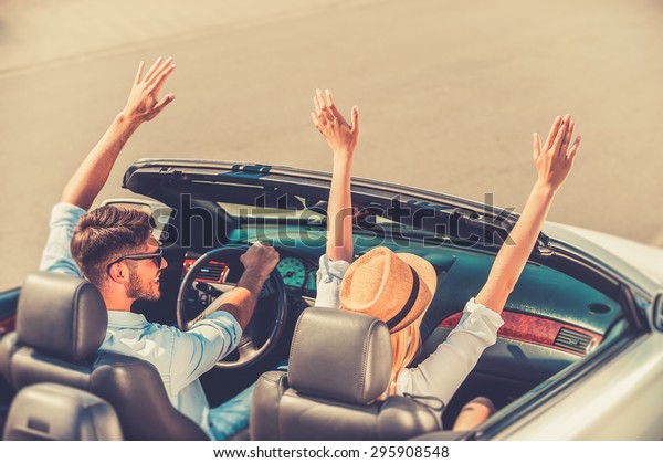 Getting\
away from it all. Top view of cheerful young couple keeping arms\
raised while riding in their white\
convertible