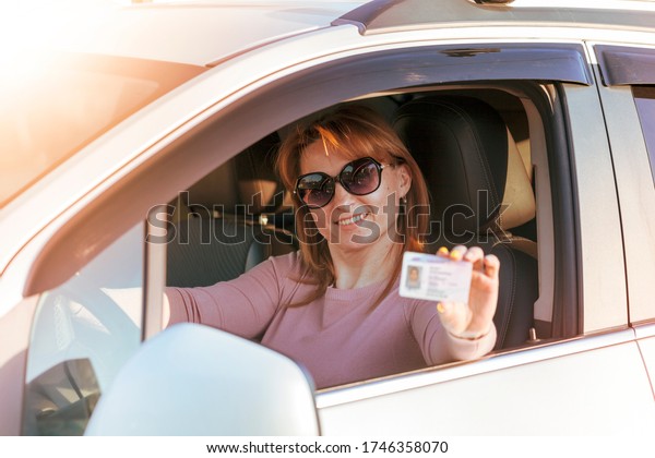 Getting a driver\'s license, a beautiful driving girl\
shows a new driver\'s license. Young woman holding driving license\
near open car. 