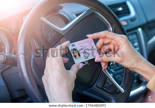 Getting a driver\'s license,\
female hands show US driving license, amid the steering wheel of a\
car