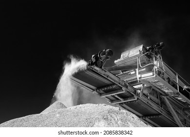 Getting a fine stone fraction on a mobile crusher, industrial equipment against a dark sky, close-up, black and white.