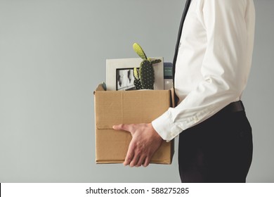 Getting fired. Cropped image of handsome businessman in formal wear holding a box with his stuff, on gray background