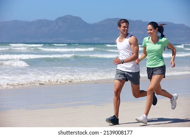 Getting Fit Together. Shot Of A Young Couple Jogging Together On The Beach.