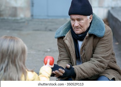 Getting food. Kind little girl gives apple to a homeless person.