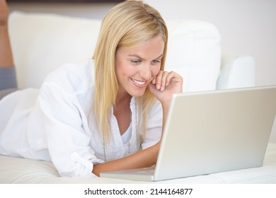 Getting The Latest News Online. A Gorgeous Young Woman Working On Her Laptop While Lying On The Sofa.