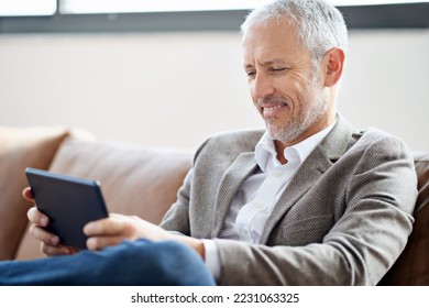 Getting the latest news online. Shot of a handsome mature man using his tablet while sitting on the sofa at home. - Shutterstock ID 2231063325