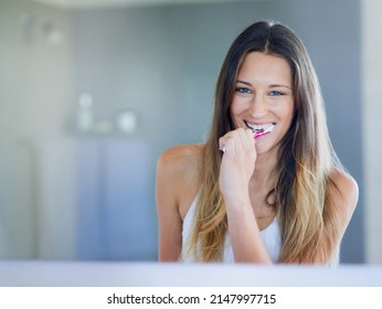 Getting Minty Fresh. Portrait Of A Happy Young Woman Brushing Her Teeth In Her Bathroom At Home.