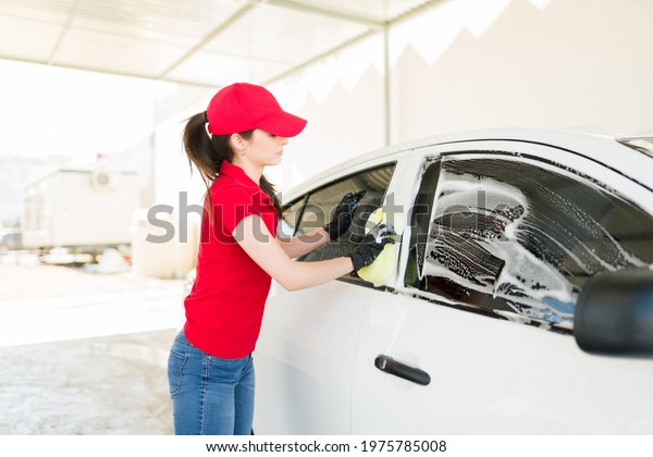 Getting my hands dirty at the car wash. Focused female\
employee with gloves using a sponge and soap to wash the car\
windows of a vehicle 