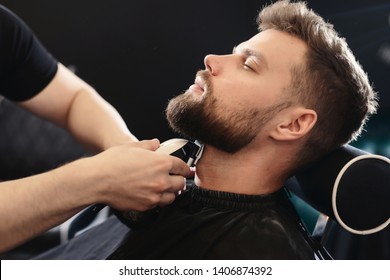 Getting perfect shape. Close-up side view of young bearded man getting beard haircut by hairdresser or barber at barbershop - Powered by Shutterstock