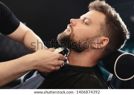Getting perfect shape. Close-up side view of young bearded man getting beard haircut by hairdresser or barber at barbershop