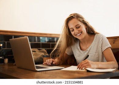 Getting Ready To Ace That Test. Shot Of A Happy Young Student Using Her Laptop To Study At A Cafe Table.