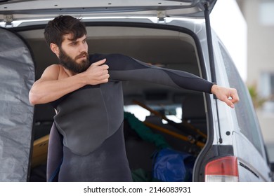 Getting Ready For An Early Surf Session. A Young Man Putting On His Wetsuit Before A Surf.