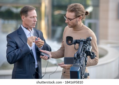 Getting Ready. Fair-haired Operator Helping Male Reporter Fit Headset