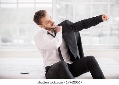 Getting Ready For New Working Day. Young Beard Man Dressing Up His Jacket While Sitting On The Bed  