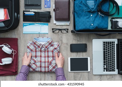 Getting ready for a trip and packing a suitcase, a man is holding his shirt before putting it into his bag, travel and vacations concept