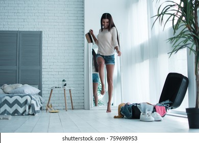 Getting ready for vacation. Full length of beautiful young woman looking carefree and positive with smile while packing her suitcase - Powered by Shutterstock