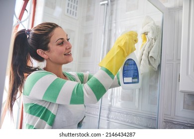 Getting rid of grease and grime. Shot of a young woman cleaning a bathroom shower door. - Shutterstock ID 2146434287