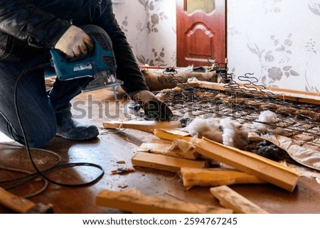 Getting rid of old things. Man disassembling an old sofa in the attic.