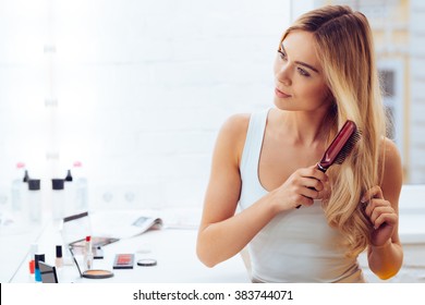 Getting Rid Of Tangles. Beautiful Young Woman Looking At Her Reflection In Mirrorand Brushing Her Long Hair While Sitting At The Dressing Table