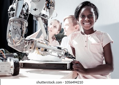 Getting Smarter Every Day. Waist Up Shot Of An African American Girl Looking Into The Camera With A Cheerful Smile On Her Face After Visiting A Work Shop And Seeing Impressive Robotic Machines.