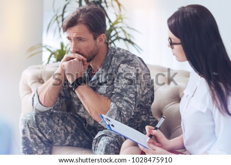 Getting through tough times. Experienced soldier sitting on a sofa and passing his military life in review while attending a female psychotherapist.