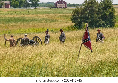 Gettysburg, PA, USA - June 14, 2008: Battlefield monuments. landscape with Group of males with Confederate flag enacting war scenery, set in beige yellow weed meadow. Barns on horizon.