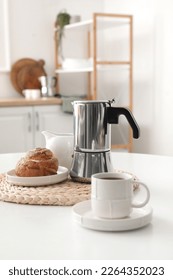 Geyser coffee maker with delicious bun and cup of espresso on table in kitchen