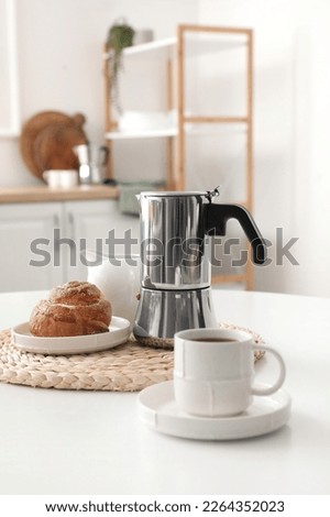 Geyser coffee maker with delicious bun and cup of espresso on table in kitchen
