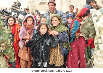 GHAZNI PROVINCE, AFGHANISTAN - February 2011: Afghan Girls Dressed In Colorful Regional Clothes Wait For Warm Clothes Provided By US And Polish Soldiers From Task Force White Eagle