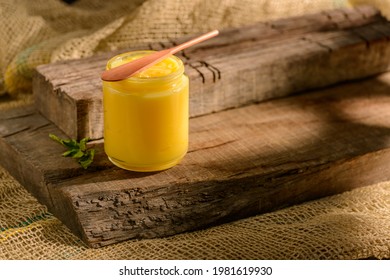 Ghee butter in glass jar with wooden spatula on wood.