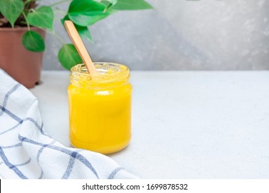 Ghee or clarified butter in a glass jar on a neutral textured background with copy space